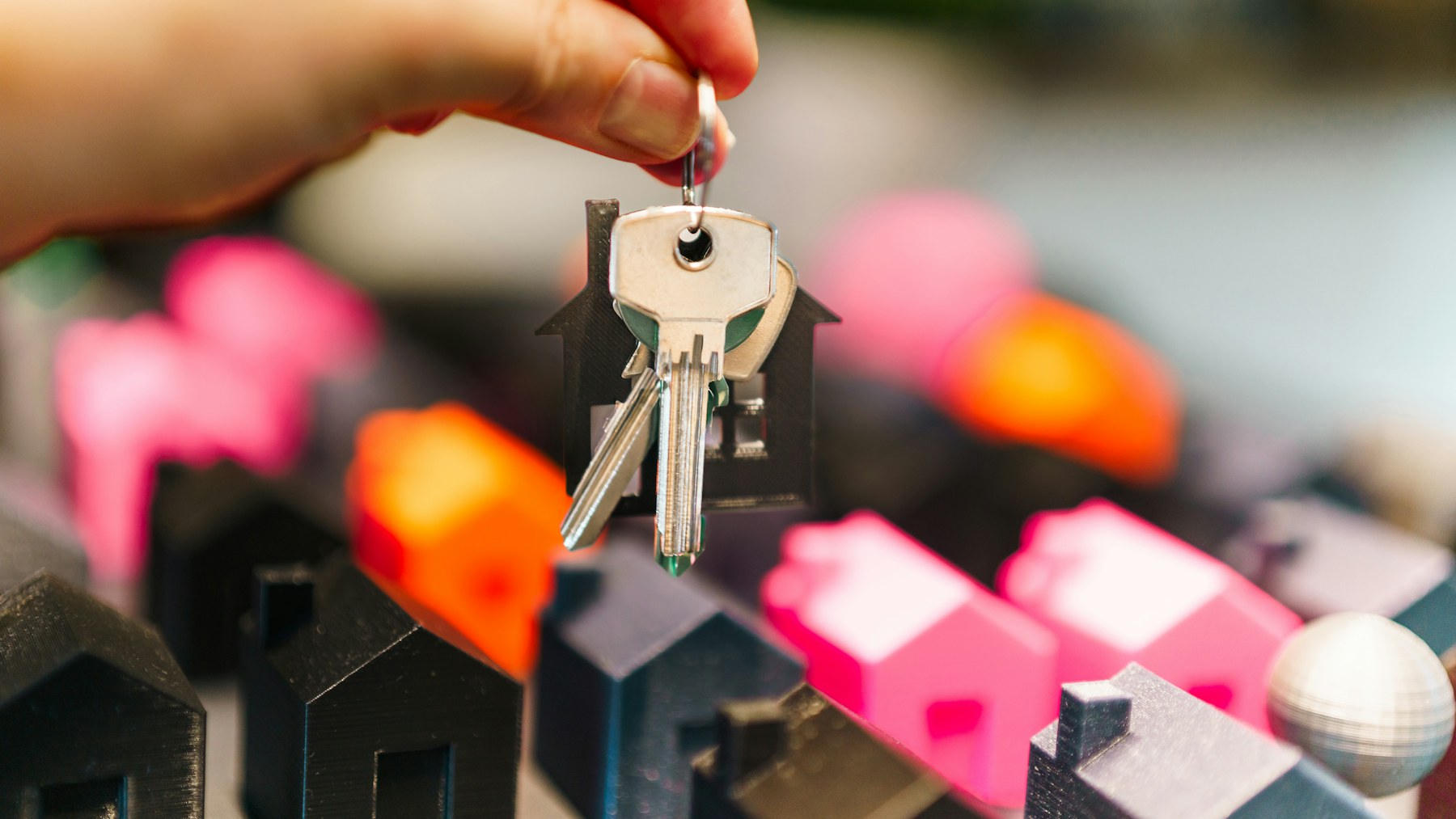 House keys held above miniature homes representing the housing market